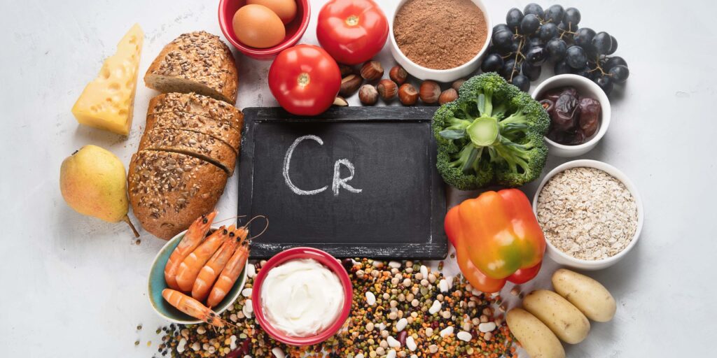 Foods high in chromium, including whole grains, broccoli, grapes, eggs, nuts, legumes, and dairy, surrounding a chalkboard marked 'Cr' for sugar cravings and insulin resistance